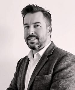 Black and white headshot of author Pete Ketchum wearing a blazer and collared shirt, looking slightly to the side.