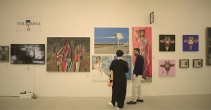 Visitors standing and discussing artworks at TERAVARNA booth, with multiple contemporary paintings displayed on a gallery wall at an art fair.