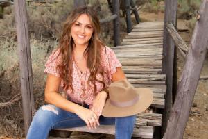 Dionya sitting on old wood bridge wearing blue jeans and pink print blouse