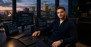 online digital marketing internship course image of confident young professional in smart casual clothing sits at a modern minimal desk in a London office with floor-to-ceiling windows showing the Canary Wharf skyline at dusk.