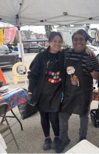 As farmers markets prepare to open across Pittsburgh, they bring more than fresh produce and weekend foot traffic—they offer one of the most accessible entry points for small businesses and first-time entrepreneurs Owners of Lula La Chula stand together smiling under a canopy at an outdoor farmers market booth, wearing aprons as they prepare and serve food