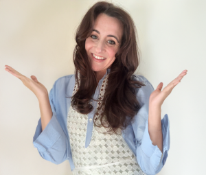 Portrait of Courtney Bierman, smiling with arms raised, wearing a blue blouse and white textured vest.
