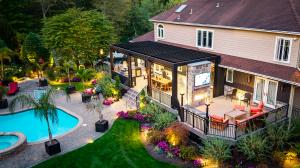Backyard with a covered deck structure, outdoor dining area, built-in fireplace with mounted TV, pool, and landscaped patio behind a residential home
