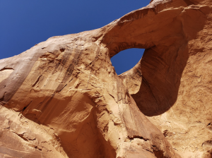 Large natural sandstone arch formation in Monument Valley with smooth red rock and a deep blue sky background.