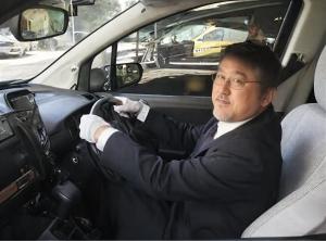 A photo of TOKA the Driver behind the wheel of his taxi in Tokyo, representing his background as a professional driver before completing his 100-day musical project.