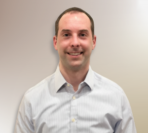 Professional headshot of Dr. Valenzano, smiling in a light blue button-down shirt against a neutral background
