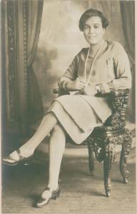 In this portrait of important African-American author, editor and mentor Jessie Redmon Fauset, she is seated in an ornate carved chair and stylishly attired in a drop-waist dress with layers of pleats. She has a long string of pearl-like beads at her neck