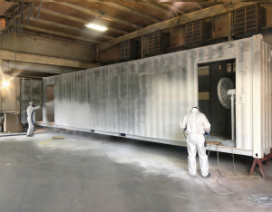ArmorThane USA Inc., a leading manufacturer of polyurea and polyurethane protective coatings, today announced it has secured more than a dozen blast mitigation contracts spanning eight countries ArmorThane-certified applicators in full PPE spray-applying polyurea coating to a large steel enclosure inside a facility — authentic jobsite application of ArmorThane blast mitigation systems