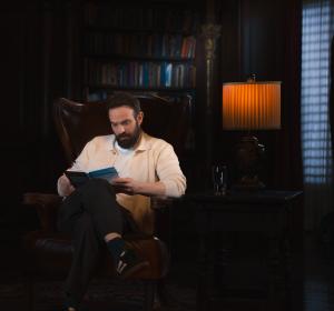 Charlie Cox sits in a high-backed leather chair, reading an annotated copy of The Razor's Edge by Somerset Maugham.