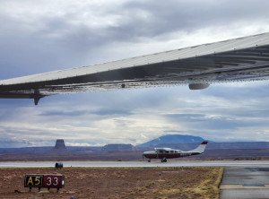Single-engine aircraft taxiing on runway at Page, Arizona (KPGA) with desert mesas and mountains in the background, viewed from beneath a wing