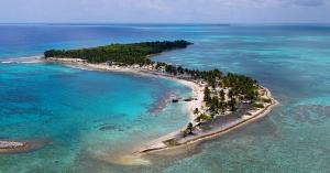 Aerival view of S-shaped island filled with palm trees and surrounded by turquoise water.
