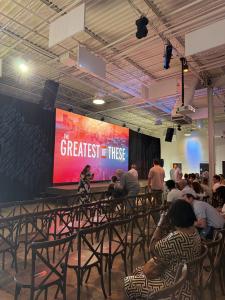 A packed audience fills the premiere venue in Atlanta on April 16, 2026 for the screening of The Greatest of These, with the film's bold red and orange title card displayed prominently on a large LED screen on stage, as guests gather to celebrate the rele