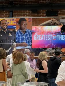 Guests gather and converse at the Atlanta premiere reception of The Greatest of These on April 16, 2026, surrounded by a striking large-scale photo wall featuring the faces of City of Refuge community members and the bold title display of the documentary