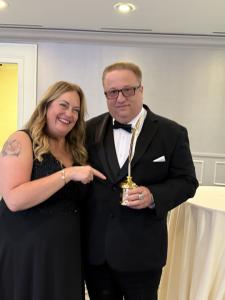 Sir Michael Fomkin, Co-Founder of VIP Ignite, dressed in a tuxedo and holding his Telly Award, poses and smiles alongside Deneen White, President of Talent Development at VIP Ignite, at an awards ceremony celebrating his recognition for excellence in ente