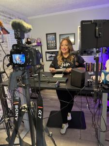 Deneen White, President of Talent Development at VIP Ignite, smiles while standing at a professional recording desk surrounded by Sony camera equipment, professional microphones, studio lighting, and production gear, capturing her commitment to creating i