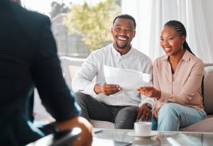Couple sitting on couch smiling, reviewing documents with insurance agent