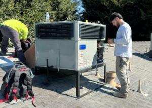 Two HVAC technicians from Arrow Appliance servicing a large grey air conditioning unit on a residential rooftop in the Central Valley.