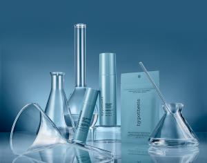 The hypothesis™ acne range — Acne Precision Serum, Daily Acne Cleanser, and Precision Microdart Blemish Patches — arranged with laboratory glassware against a blue gradient background, reflecting the brand's precision enzyme science positioning