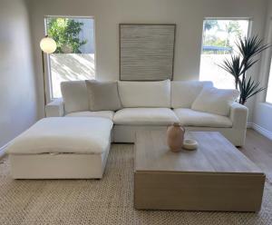 White Mirewood modular cloud sofa with washable removable covers, shown in a sectional configuration with separate ottoman in a bright modern living room with natural light.