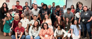 The Zarrow Institute on Transition & Self-Determination Strengthens Commitment to Accessibility with CAC Renewal 18 Group photo of diverse adults in a classroom setting, some seated and others standing, with a presentation screen in the background.