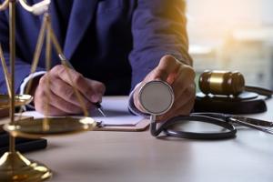 The American Institute of Health Care Professionals Offers a Medical Malpractice Consulting Certification Program 20 photo a medical malpractice consultant in a business suit sitting writing a report with a stethscope at the desk and the scales of justice as well