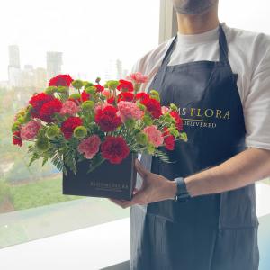 Florist holding a luxury flower box arrangement with red and pink carnations and green button chrysanthemums.