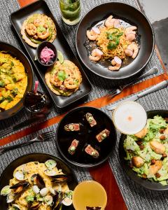Overhead flatlay of GigiO Restaurant Puerto Viejo Costa Rica lunch and dinner menu featuring shrimp tostadas, seared tuna tataki, linguine with mussels and clams, shrimp noodle bowl, yellow seafood curry, chicken Caesar salad, and tropical craft cocktails
