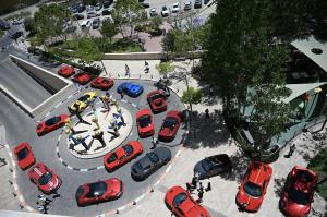 The roar of high-performance engines is a sound usually reserved for professional racetracks or coastal highways A breathtaking aerial view of the Shalva National Center courtyard, where a fleet of vibrant Ferraris surrounds the iconic Shalva statue. The image captures the striking contrast between world-class automotive engineering and the heart-warming symbol of i