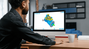 saVRee has expanded its VR/AR content to support remote maritime learners Man viewing 3D blue and yellow pump CAD model on computer screen at office desk.