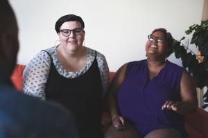Two diverse women seated together in conversation in a warm, plant-filled space, representing the integrated therapeutic community at Asana Recovery's LGBTQ+ specialty program.