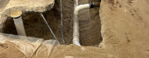 A professional plumbing repair site showing an excavated section of a concrete foundation with newly installed white PVC piping and connections, illustrating a slab leak repair service by KPS Plumbing in Bakersfield