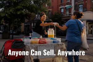 Young Latina woman smiling as she hands food to a customer across a folding table on a city street corner, selling empanadas with a handwritten cash-only sign, text overlay reads