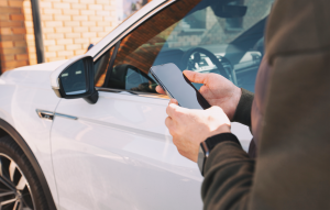 Osoba koja koristi pametni telefon pored rabljenog automobila, predstavlja provjere povijesti vozila Car Owl za vozače iz Ujedinjenog Kraljevstva koji razmišljaju o rabljenim električnim automobilima.