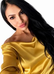 Portrait of international fashion editor Giulia Deamina wearing a gold satin off shoulder top against a light background.