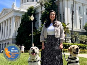 Woman standing with two working guide and service dogs with California State Capital in background.