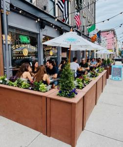 Guests dining under white umbrellas on the sidewalk patio at The Courtside Biergarten outside Courtside Bar & Grill in Downtown Binghamton.