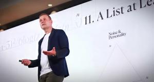 Change management speaker Chris Hirst delivering a keynote on stage in front of a large presentation screen.