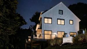 A home at night with lights on surrounded by trees and landscaping against a dark sky with stars. A new Generac Next Gen Generator model at the lower right keeps the power on through an outage.