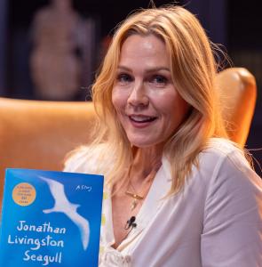 Jennie Garth smiles, holding a copy of Jonathan Livingston Seagull
