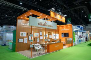 The garden of naturalsolution exhibition booth at in-cosmetic Asia trade show featuring wooden panels, orange structural design, botanical displays, and sustainability messaging for cosmetics industry