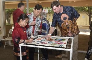 People of all ages jointly painting a batik (dye ink on cloth with wax resist) artwork