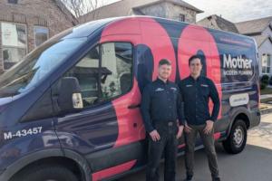 2 uniformed plumbers from Mother Modern Plumbing pose with service van outside Dallas, TX home