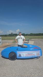 Aaron Novinger standing next to a blue human-powered velomobile, promoting a charity bike ride from Dallas to Washington, D.C. to raise awareness for Ponzi victims through PonziRelief.org