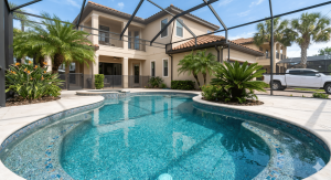 Beautiful backyard pool area with tropical plants and modern home, featuring a screened enclosure and clear blue water.