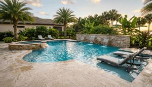 Luxurious backyard with a stone-edged pool, waterfall features, and palm trees. Poolside lounge chairs offer a relaxing tropical ambiance at sunset.