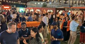 Crowd networking at the evening Boston AI Week Opening Party held at Island Creek Raw Bar in WS Development's Seaport in Boston. Lined with string lights and vendor stalls