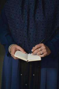 west asian woman in blue abaya carrying a notebook and pen with elegant golden accents