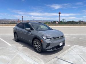 Envoy Technologies Inc. ( A gray Volkswagen ID.4 electric SUV parked in a lot at Valencia by FivePoint, with Six Flags Magic Mountain roller coasters and the surrounding mountains visible in the background.