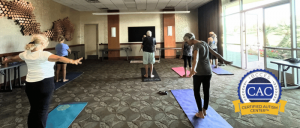 A group of adults practicing yoga on mats in a well-lit room with large windows and a 