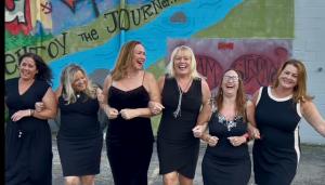 six ladies locked arms in black dresses walking and laughing together